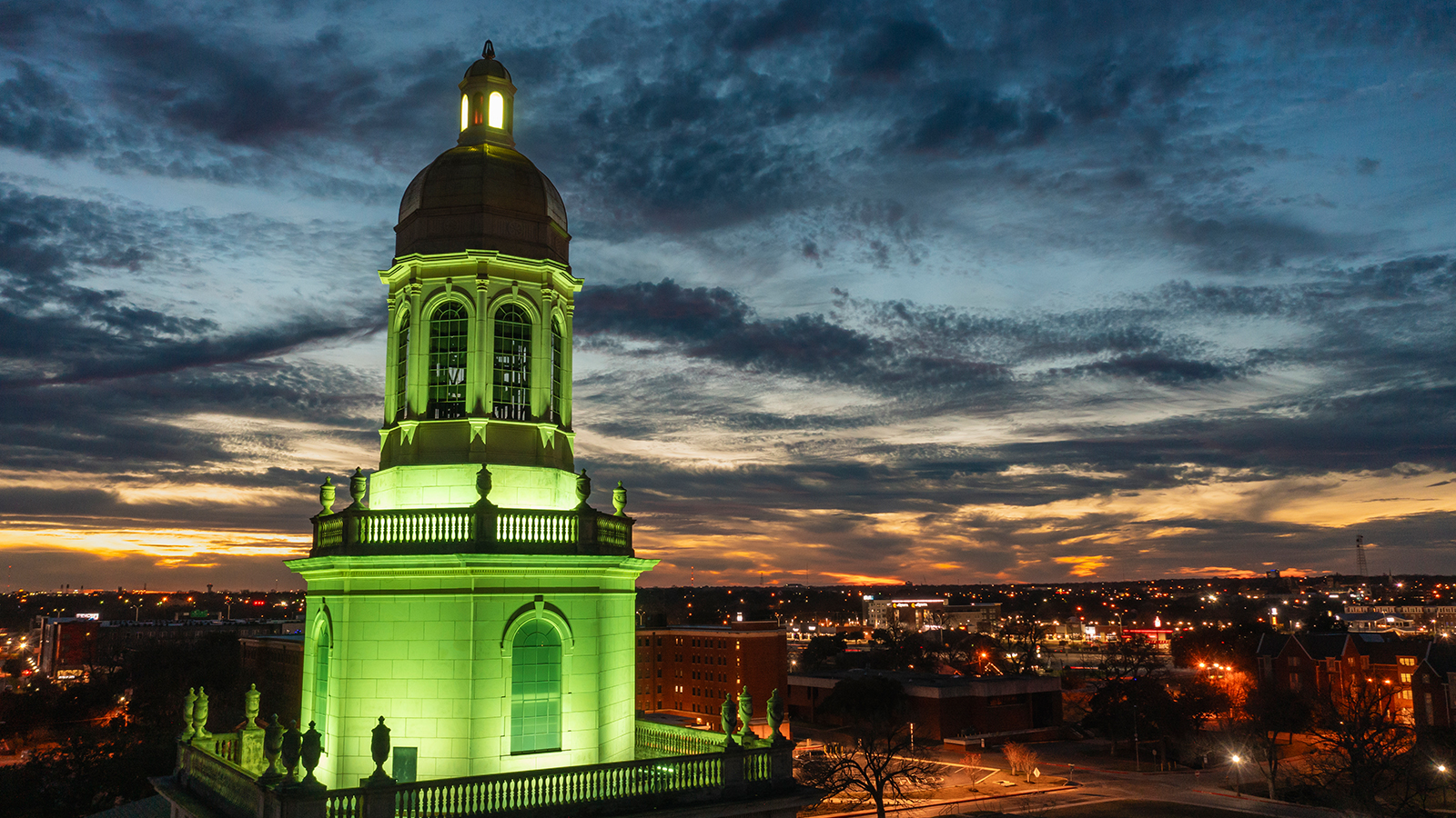 Baylor University's Pat Neff Hall is lit up green, with sunset in background.