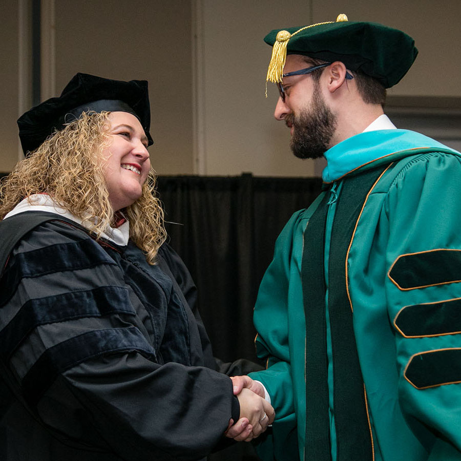 Professor shaking the hand of a doctoral graduate at their hooding ceremony.