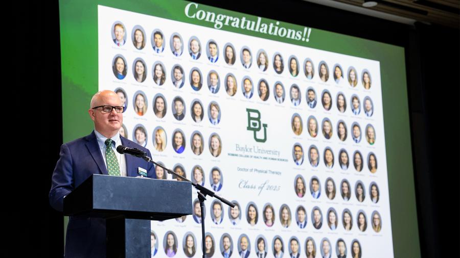 Baylor DPT Department Chair speaks at 2025 graduation banquet, with portraits of all graduates behind him on large screen.