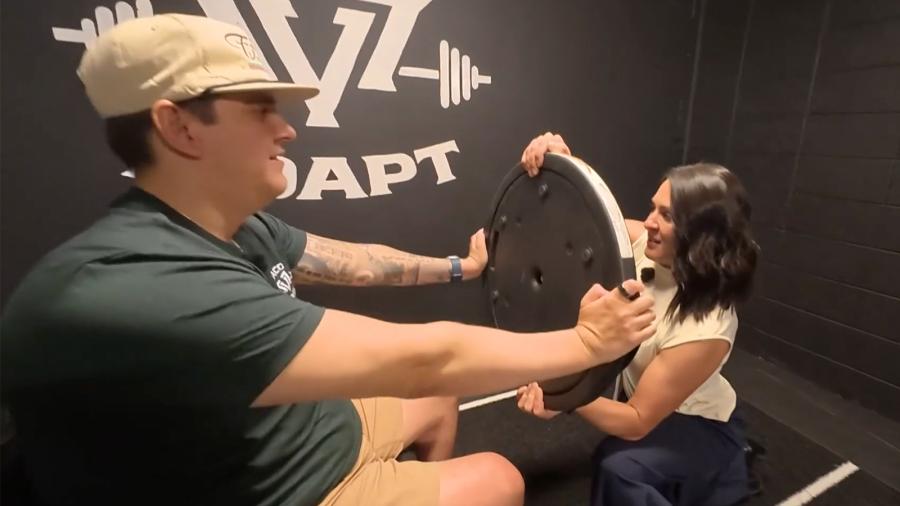 A man, sitting, works out with a weight at an adaptive gym.